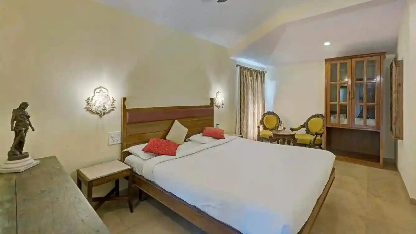 Spacious bedroom in Ramsukh Resort's family suite with a king-size bed, antique chairs, and warm lighting.