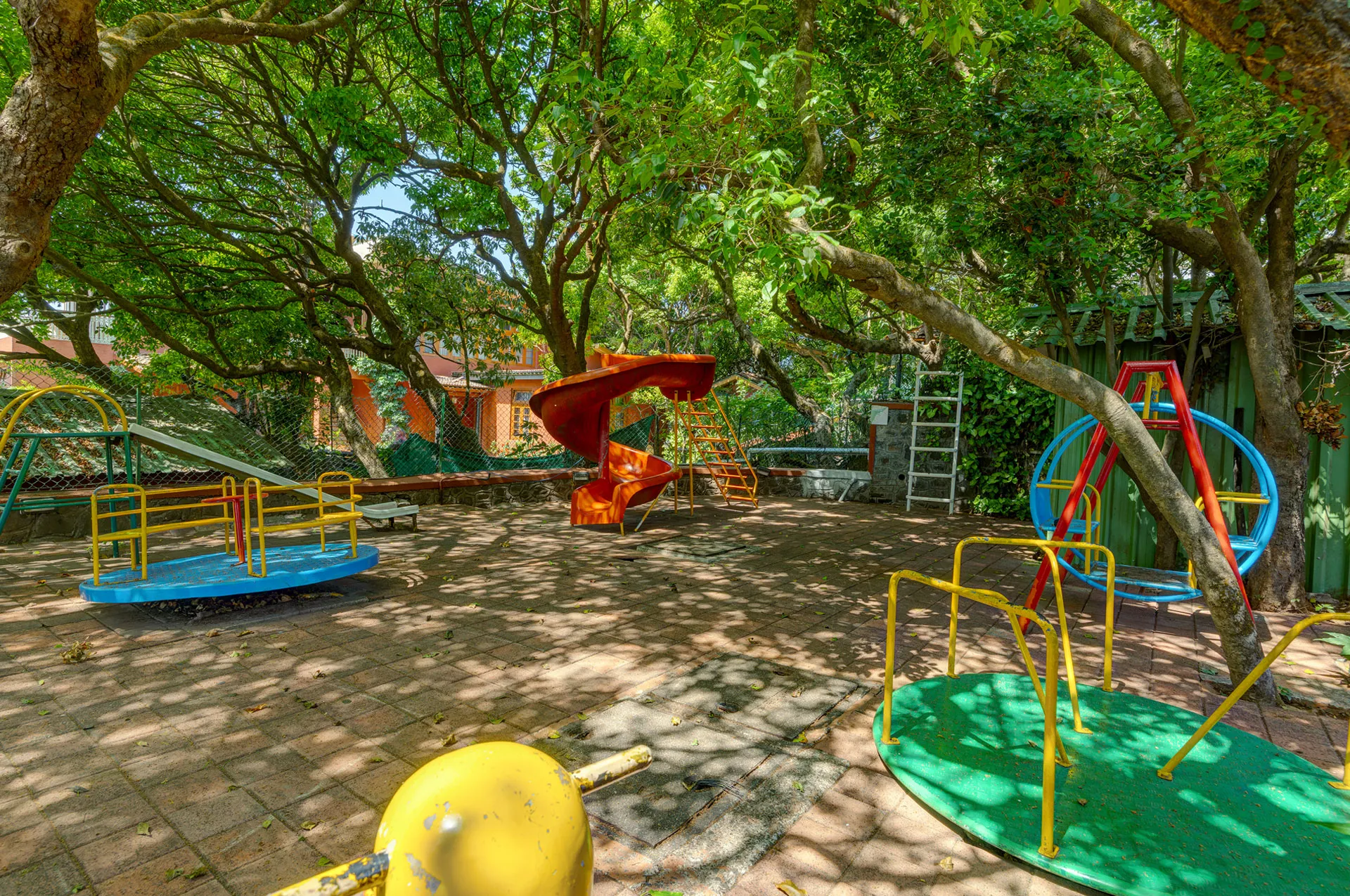 A well-shaded outdoor fitness zone at Ramsukh Resort, set amidst greenery, featuring exercise machines for physical activity in a natural setting.